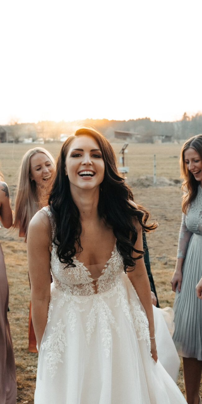 Die Braut lacht glücklich, umgeben von ihren Freundinnen in stilvollen Kleidern, während die Abendsonne die Hochzeit in warmes Licht taucht.