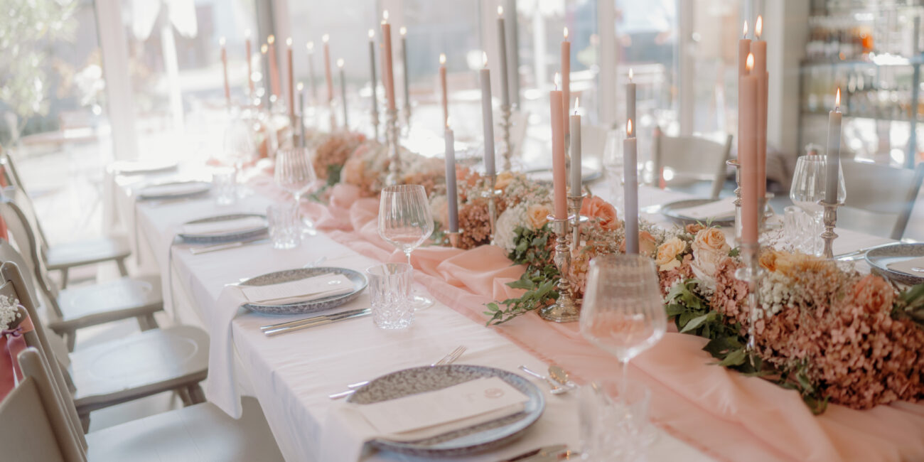 Stilvoll gedeckter Hochzeitstisch mit rosa Tischläufer, Kerzen und Blumenarrangements in warmen Farbtönen.