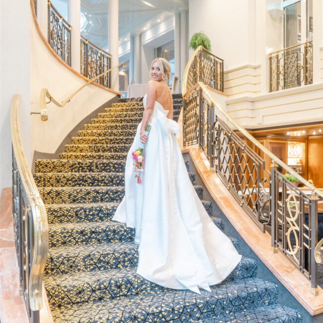 Die strahlende Braut posiert elegant auf einer luxuriösen Treppe und blickt glücklich zurück.