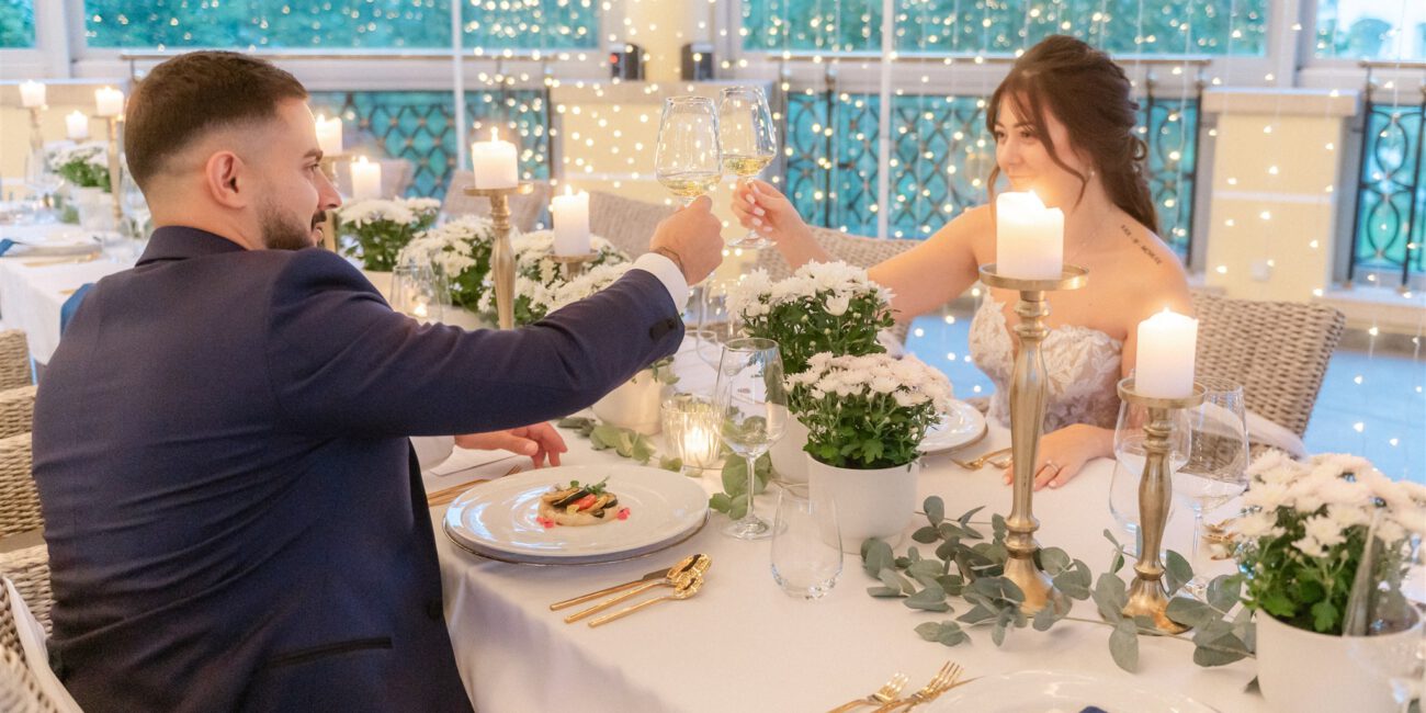 Brautpaar stößt bei romantischem Hochzeitsdinner mit Kerzenlicht an.